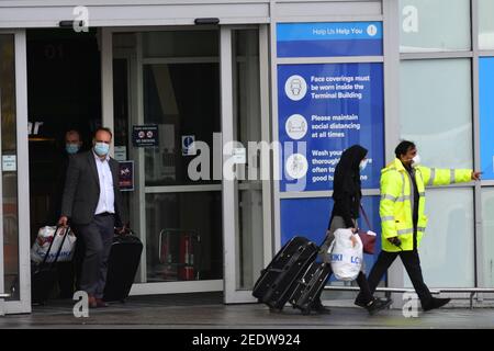 Nach der Landung in England verlassen zwei Passagiere den Flughafen Birmingham an Bord eines Busses. Neue Vorschriften, die jetzt in Kraft sind, verlangen, dass jeder, der sich vor kurzem an einem Ort mit hohem Risiko befindet, über einen bestimmten Hafen nach England einreist und ein Paket im Voraus gebucht hat, in einer der von der Regierung verwalteten Quarantäneeinrichtungen übernachtet. Bilddatum: Montag, 15. Februar 2021. Stockfoto