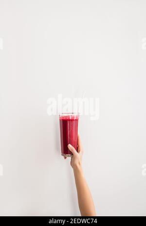 Menschliche Hand hält Glas mit lila Rüben Granatapfel frischen Smoothie mit Glasstroh über weißen Wand Hintergrund, kopieren Raum. Detox, Diät, Gewichtsverlust, gesunde Lebensweise Konzept Stockfoto