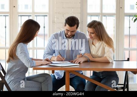 Glückliche junge Kunden Unterzeichnung Papier Vertrag mit professionellen Makler. Stockfoto