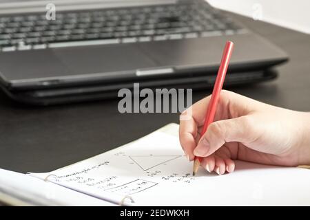 Junges Mädchen - weibliche Studentin schreibt Hausaufgaben aus Mathematik zu Hause. Er schreibt mit Bleistift in ein Notizbuch und zählt Formeln. Stockfoto