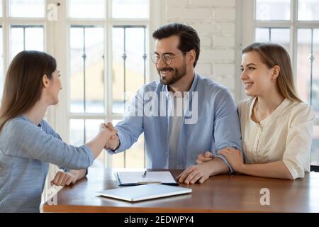 Glückliches junges Familienpaar schüttelt sich die Hände mit Immobilienmakler. Stockfoto