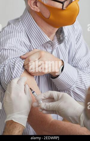 Vertikale Nahaufnahme eines nicht erkennbaren Arztes, gegen den ein älterer Mann impft Covid 19 in der medizinischen Klinik Stockfoto