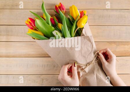 Der Prozess der Verpackung Bouquet von frischen Tulpen in umweltfreundliche Handwerk Papier. Schritt 3. Geschenk für Frühlingsferien. Blumengeschäft. Stockfoto