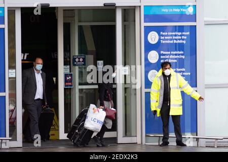 Nach der Landung in England verlassen zwei Passagiere den Flughafen Birmingham an Bord eines Busses. Neue Vorschriften, die jetzt in Kraft sind, verlangen, dass jeder, der sich vor kurzem an einem Ort mit hohem Risiko befindet, über einen bestimmten Hafen nach England einreist und ein Paket im Voraus gebucht hat, in einer der von der Regierung verwalteten Quarantäneeinrichtungen übernachtet. Bilddatum: Montag, 15. Februar 2021. Stockfoto