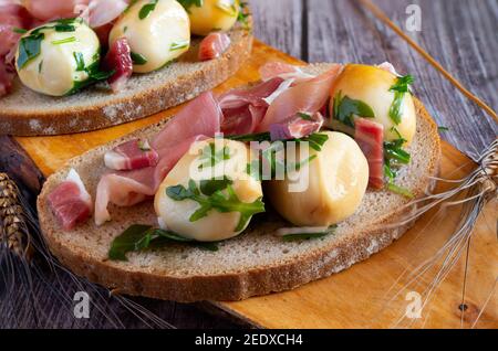 Snack-Vorspeise mit Vollkornbrot, rohem Schinken und geräucherten Provola-Kugeln in Öl Stockfoto