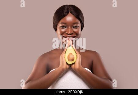 Portrait der jungen schönen afroamerikanischen Frau hält reif frisch Avocado halb Stockfoto