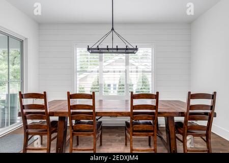 Ein modernes Bauernhaus Esszimmer mit einer Shiplap Wand, einem großen Holztisch mit Stühlen und Sitzbank, und einem großen schwarzen Kronleuchter. Stockfoto