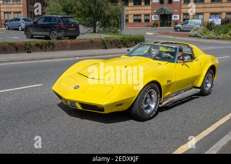 Eine gelbe 1973 Corvette stingray, die an Bürogebäuden vorbeifährt Das Vereinigte Königreich im Frühlingssonne Stockfoto