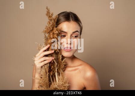 Eine schöne junge Frau mit zurückgezogenem Haar hält ein trockenes Pampagras in ihren Händen. Das Konzept der Naturkosmetik aus Weizenkörnern. Hautpflege Stockfoto