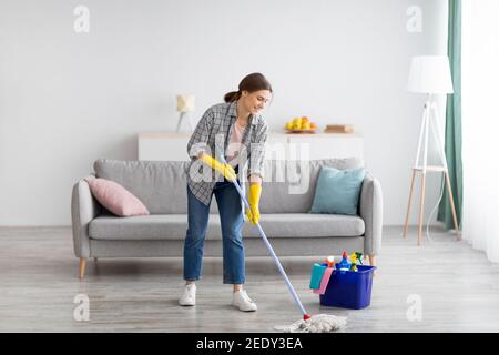 In voller Länge Porträt von glücklich junge Frau wischen Boden im Wohnzimmer, kopieren Raum Stockfoto