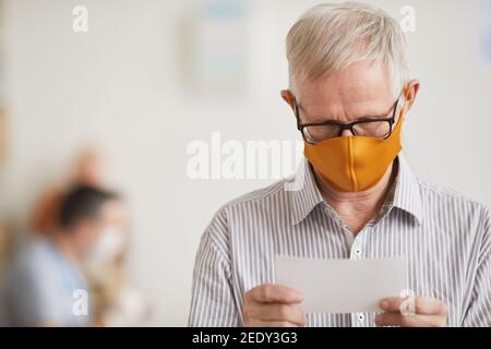 Porträt von weißhaarigen älteren Mann trägt Maske und Lesen Verschreibungspflichtige Notiz an der Arztpraxis in der medizinischen Klinik Stockfoto