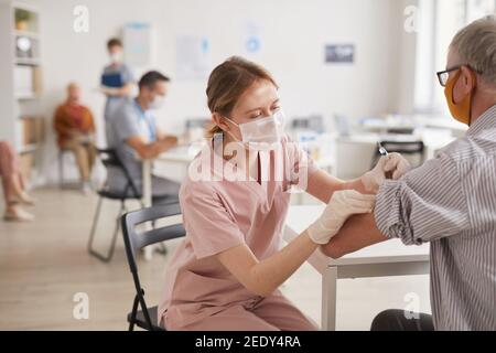 Porträt einer jungen Ärztin, die einen älteren Mann impft, im Impfzentrum oder in der medizinischen Klinik, Kopierraum Stockfoto