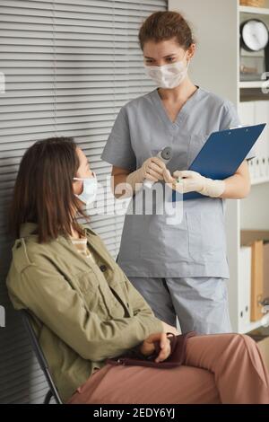Vertikales Porträt der jungen Ärztin im Gespräch mit dem wartenden Patienten In der Linie in der medizinischen Klinik oder Impfzentrum Stockfoto