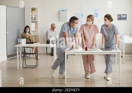 In voller Länge Porträt von drei Ärzten mit Masken stehen am Schreibtisch in der medizinischen Klinik, kopieren Raum Stockfoto