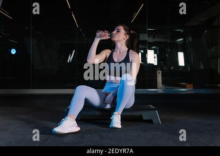 Die Sportlerin sitzt auf der Trittsowie und blickt auf die Kamera. Sie hat eine Wasserflasche in der Hand. Stockfoto