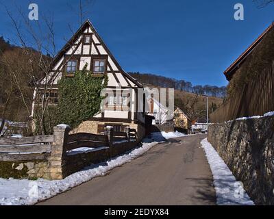 Historisches Fachwerkhaus mit Holzzaun, Steinmauer und asphaltierter Straße im kleinen ländlichen Dorf Gundelfingen, Teil von Münsingen, Deutschland. Stockfoto