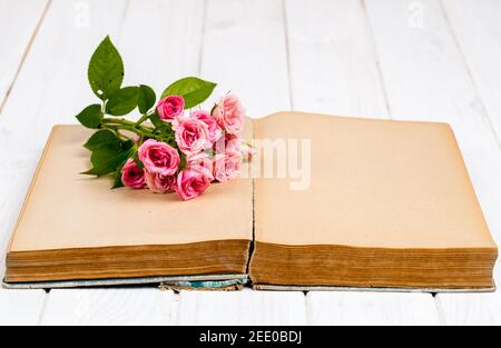 Rosen auf einem alten Buch auf weißem Holzhintergrund. Blumen und Stockfoto