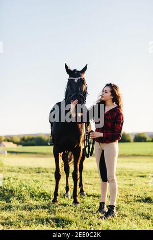 Junge Frau gekleidet lässig streicheln schwarzes Pferd. Tierische und menschliche Freundschaft. Stockfoto