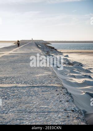 Seeufer mit feinem weißen Sand, der durch den Schneesturm zieht Auf einer asphaltierten Straße Stockfoto