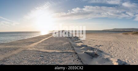 Meeresküste mit feinem weißen Sand, der durch den Schneesturm zieht Auf einer Asphaltstraße bei Sonnenuntergang Stockfoto