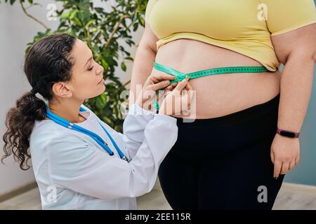 Ernährungsberater inspiziert eine Frau die Taille mit einem Maßband, um eine Gewichtsabnahme Ernährung zu verschreiben. Fettleibigkeit, ungesundes Gewicht Stockfoto