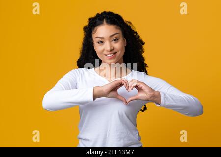 Schöne junge schwarze Dame macht Herz Geste mit Händen in der Nähe Brust Stockfoto