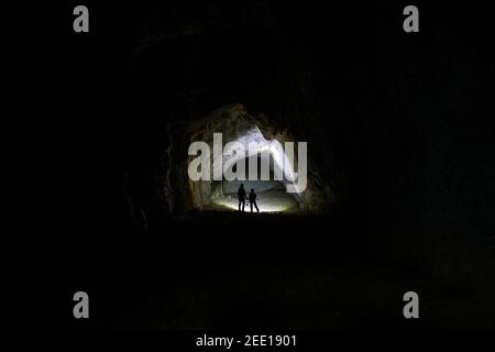 Silhouette von Mutter und Sohn, die in einer Höhle mit einer Petroleumlampe in der Hand stehen, beleuchtet von einer Hintergrundbeleuchtung, Slowenien Stockfoto