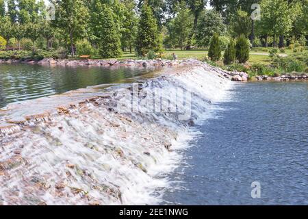 Das Fragment des Sees im Landschaftspark Meschyhirja bei Kiew, Ukraine. Im Vordergrund sieht man einen wunderschönen künstlichen Wasserfall. Stockfoto