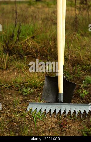 Rechen und Schaufel wird in den Boden für die Bepflanzung im Frühjahr eingesetzt. Frühling, Gartenpflanzen, Arbeiten auf einem Grundstück, Landschaftsbau, Gartenbau, Stockfoto