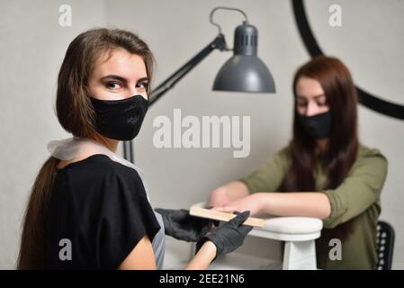 Porträt von Manikurist in einer Schutzmaske und Handschuhe bei Arbeiten Sie mit einem Kunden zusammen Stockfoto