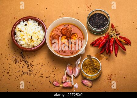 Madras-Kürbis, Basmati-Reis in einer kleinen Schüssel, ein paar trockene rote Chili-Paprika und Zwiebeln, Sesam und Bockshornklee in Arrangemet auf braunem Hintergrund. Stockfoto