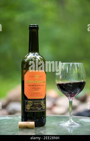 Ein Glas Rotwein auf einem Tisch im Freien, neben der Flasche und dem Korken. Stockfoto