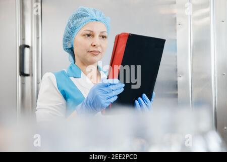 Weibliche Fabrikarbeiterin mit Computer Überprüfung Produktionslinie Getränke Produktion Molkerei Fabrik. Stockfoto