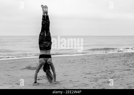 Schwarz-weiße Sportlerin, die am Strand Hand hält.Rückansicht einer nicht erkennbaren Frau am Meer beim Trainieren, Yoga üben, Bala trainieren Stockfoto