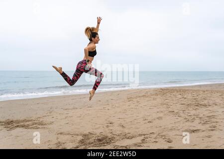 Sportliche kaukasische junge Frau springen am Strand üben Yoga .working out, Trainingskonzept, Glück und Lächeln während Übungen Lebensstil Stockfoto