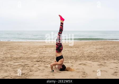 Junge fit attraktive Frau praktiziert Yoga Kopfstand Pose, salamba sirsasana pose.Athletic Frau draußen trainieren, am Strand am Meer, Leben Stockfoto