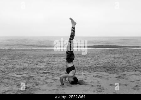 Schwarz und weiß Young fit Attraktive weibliche Ausübung Yoga Kopfstand Pose, salamba sirsasana posture.Athletic Frau trainieren, im Freien am Strand Stockfoto