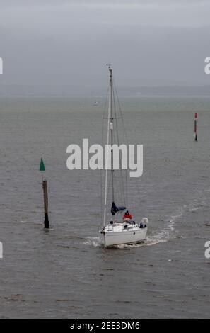 Ein Segler am Steuer einer großen Segelyacht, die mit den Segeln nach unten fährt und am Hafen im lymington solent New Forest in die Marina einfährt, Stockfoto