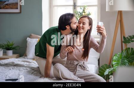 Junges Paar, das Selfie am Morgen auf dem Bett drinnen zu Hause. Stockfoto