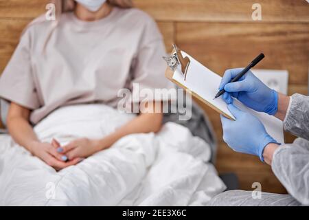 Arzt fragt weibliche Patienten über den Gesundheitszustand, professionelle Arzt Notizen, covid-19. Aufenthalt zu Hause Konzept während Coronavirus Pandemie und sel Stockfoto