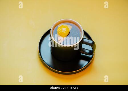 Zitronentee. Schwarzer Tee mit Zitrone auf gelbem Hintergrund. Tee mit einer Zitronenscheibe in einer schwarzen Tasse Stockfoto