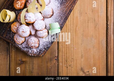 Gebackene castagnole mit Puderzucker und Konfetti auf einem Holztisch. Street Food, runde Kekse mit Zucker für den Karneval von Venedig. Traditionelles süßes Gebäck während des Karnevals. Platz zum Kopieren Stockfoto