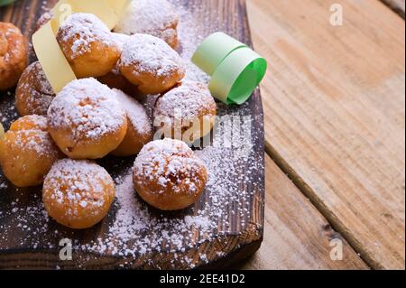 Gebackene castagnole mit Puderzucker und Konfetti auf einem Holztisch. Runde Kekse mit Zucker für den Karneval von Venedig. Traditionelles süßes Gebäck während des Karnevals. Platz zum Kopieren Stockfoto