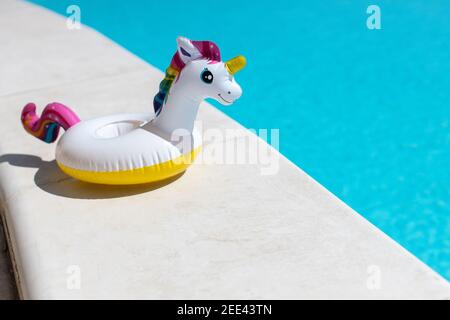 Aufblasbares pinkes Mini-Regenbogen-Einhorn, Cocktail-Stand in der Nähe von Schwimmbad an hellen sonnigen Tag, Kopierraum. Konzept Sommerurlaub, Unterhaltung, Wasser Stockfoto