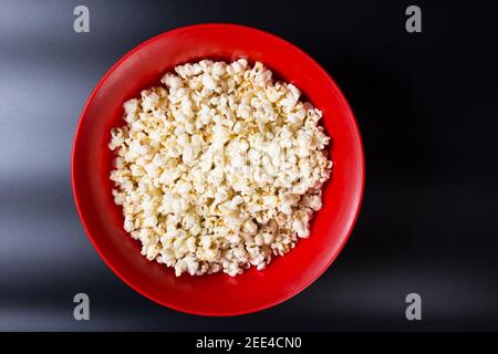 Popcorn in roter Schüssel Nahaufnahme, auf schwarzem Hintergrund. Stockfoto