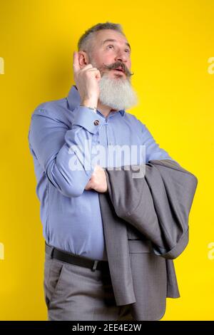 Studio Portrait reifen bärtigen Mann in grauem Anzug gekleidet sieht pensiv beiseite, denkt über etwas, gelben Hintergrund Stockfoto