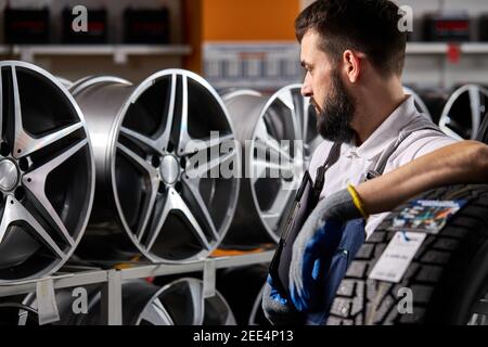 Erwachsene Auto Mechaniker Mann in Uniform haben Ruhe nach harten Arbeitstag, stehen durch Rack von Auto Räder. auto, Auto, Transportkonzept Stockfoto