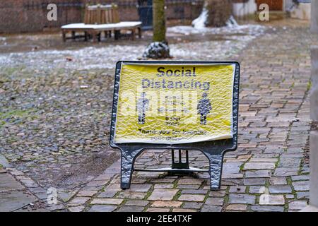 LONDON, ENGLAND - 8. FEBRUAR 2021: Gelbes öffentliches Hinweisschild, das die Menschen daran erinnert, in London bei einer Erkältung eine soziale Distanzierung zu praktizieren, die mit Schnee bedeckt ist Stockfoto