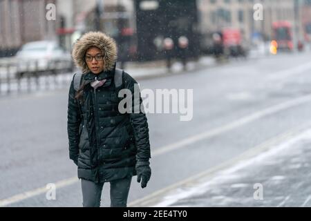 LONDON, ENGLAND - 8. FEBRUAR 2021: Entschlossene junge orientalische Frau in einer mit Pelzbesatz bekleidten Kapuze mit Brille bei einer Schneedusche in Holborn London Stockfoto