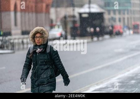 LONDON, ENGLAND - 8. FEBRUAR 2021: Schöne junge orientalische Frau in einer mit Pelz getrimmten Kapuze mit Brille beim Schneeschauer in Holborn London auf Stockfoto